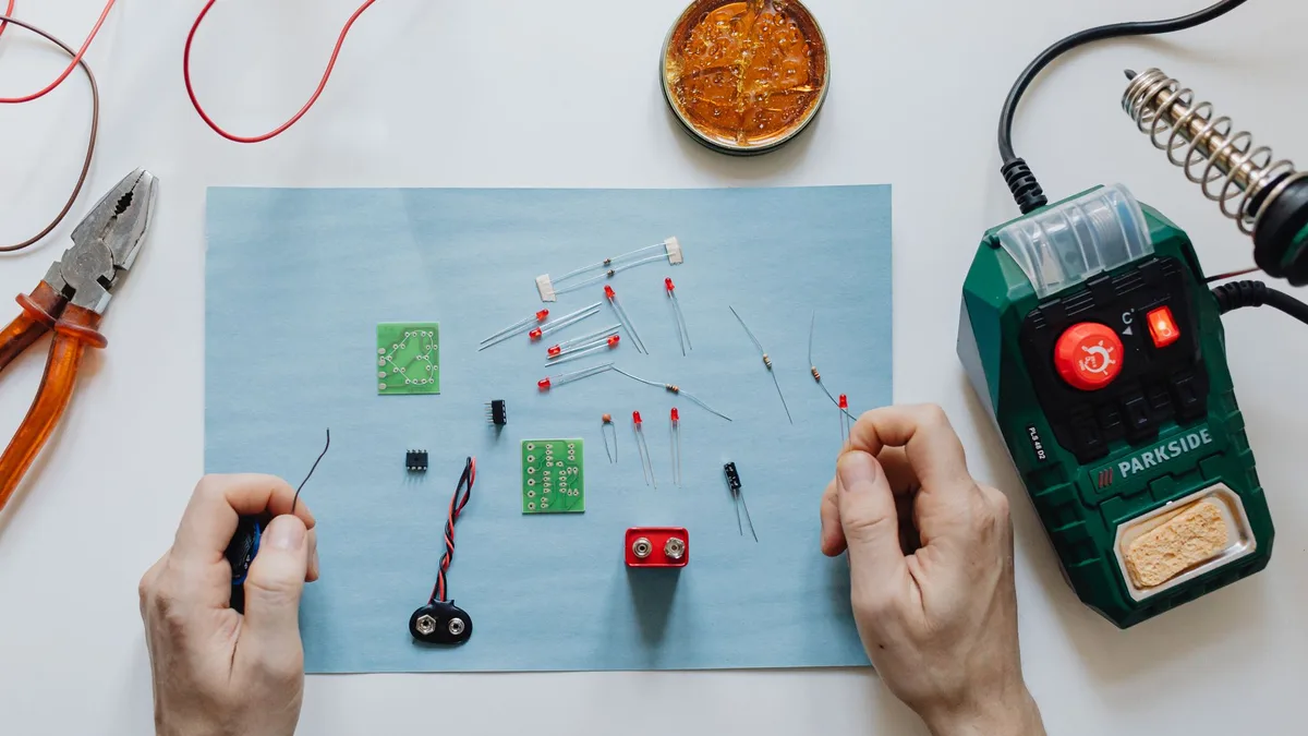 Hands-on electronics repair with tools, circuit board, and soldering station on workspace.