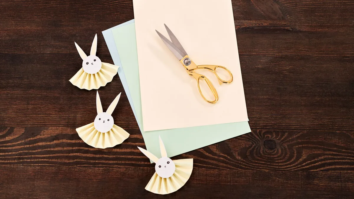 Top view of paper bunny crafts and scissors on wooden surface, perfect for Easter DIY projects.
