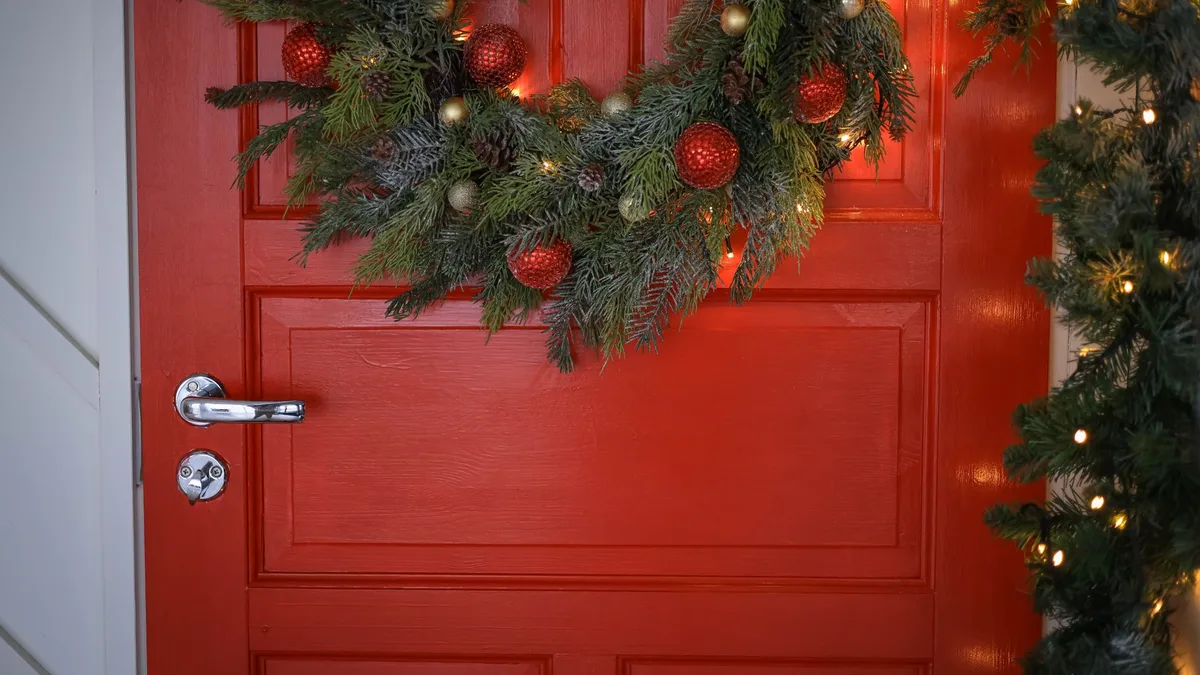 Red door adorned with a festive Christmas wreath and twinkling lights, creating a warm holiday entrance.