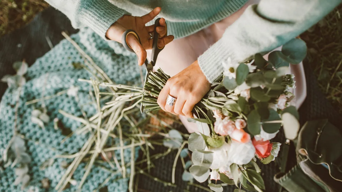 Hands trimming a bouquet with scissors, showcasing floral arrangement skills.