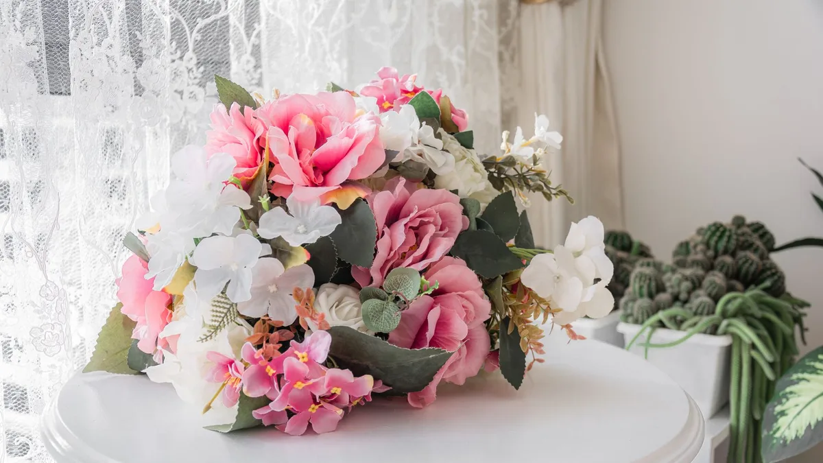 Bright artificial floral arrangement with pink and white flowers on a round table indoors.