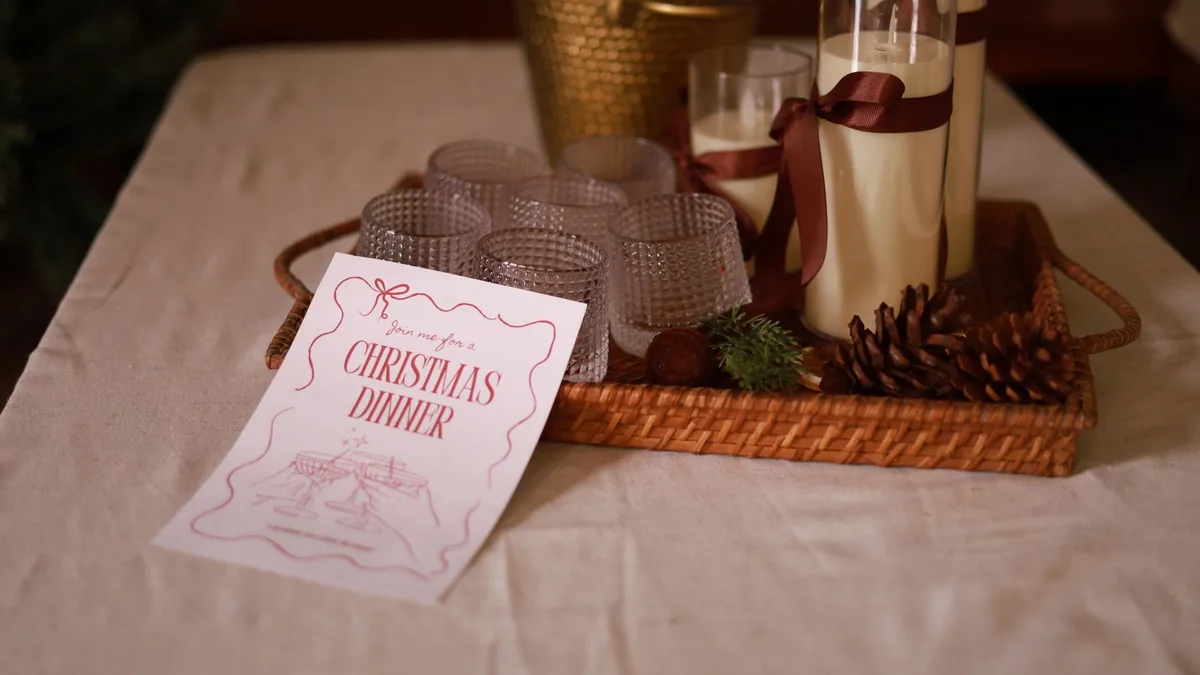 Cozy Christmas dinner invitation with candles and pinecones on a table.