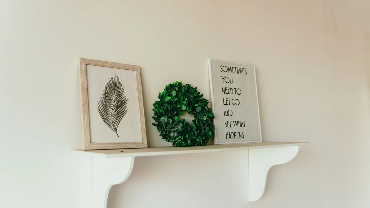 A minimalist shelf with framed art, a green wreath, and an inspirational quote.