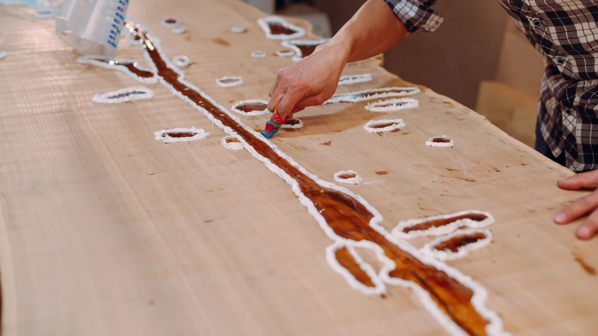 A skilled craftsman applying resin on a wooden table in a workshop setting.