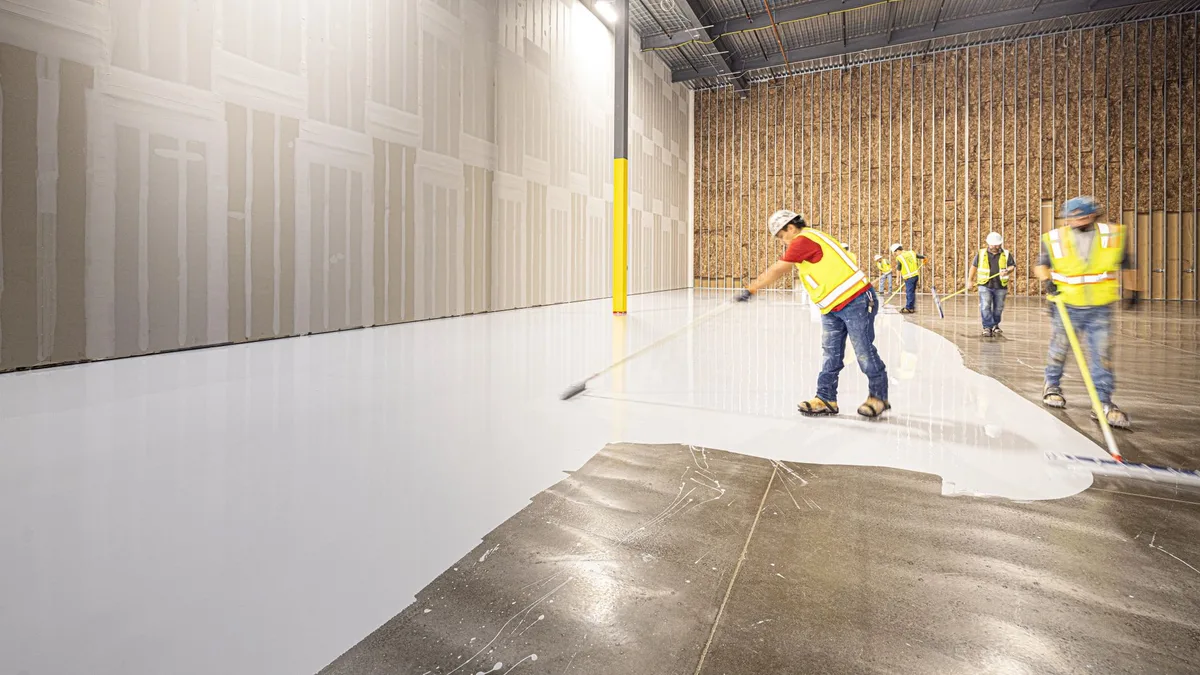 Construction workers in hard hats and vests laying a fresh concrete floor inside a building in Dallas, Texas.