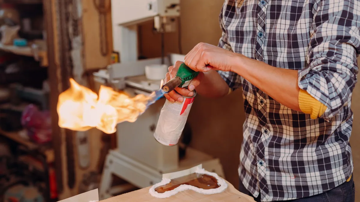Closeup of an artisan using a blowtorch to work on epoxy resin in a workshop.
