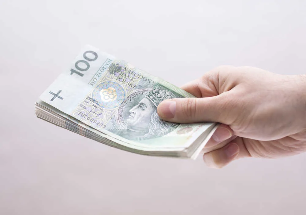 mężczyzna trzyma polskie pieniądze w banknotach w prawej ręce